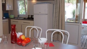 Eine kleine Küche mit Kühlschrank, Mikrowelle und Herd. Ein Esstisch mit Stühlen und einer Obstschale sind ebenfalls vorhanden.
