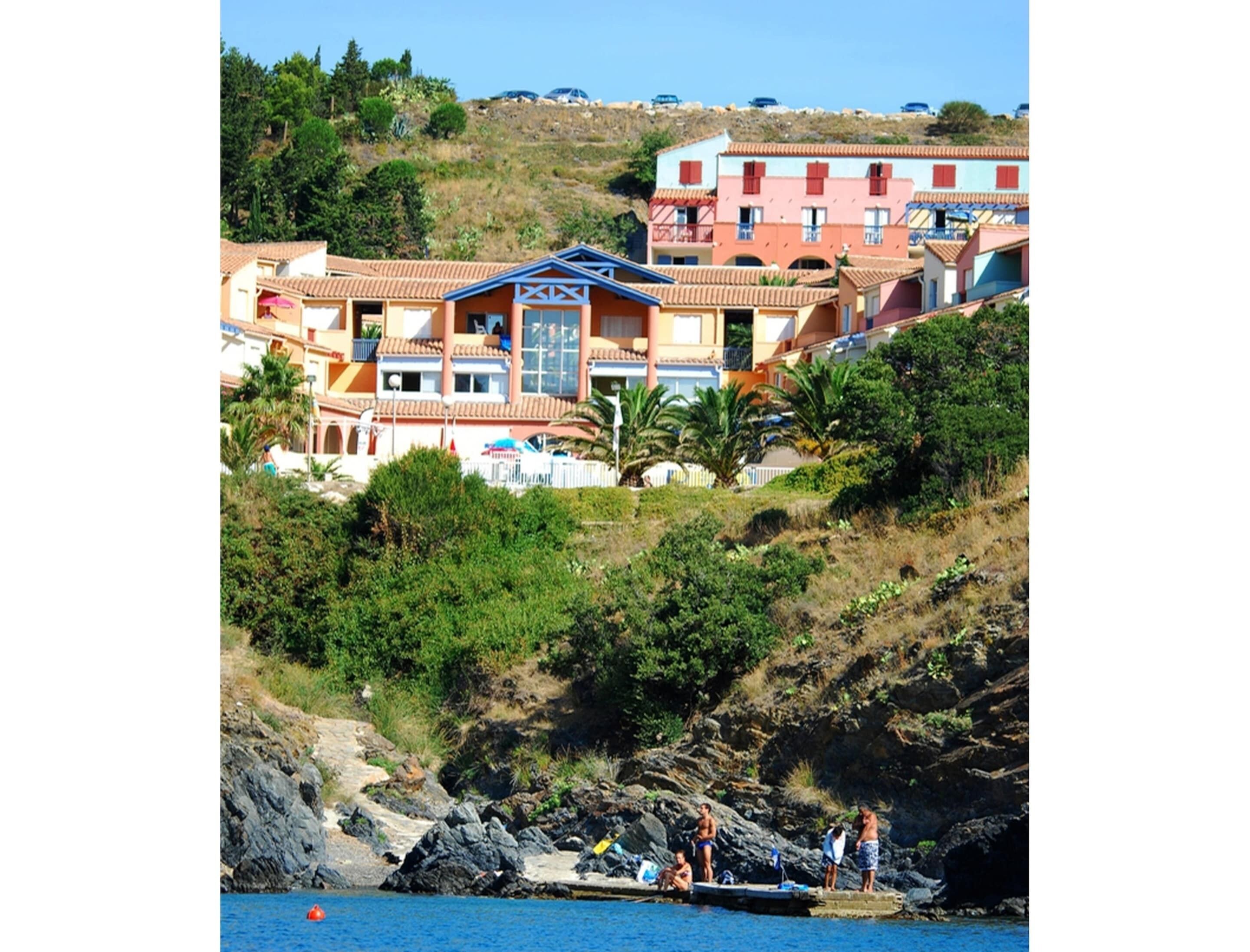 A coastal hotel with multiple buildings, a rocky shoreline, and a clear blue sky.