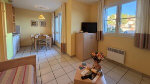 Ein kompakter Wohnbereich mit Essplatz, Küchenzeile, Fernseher und einem Fenster mit Vorhängen.