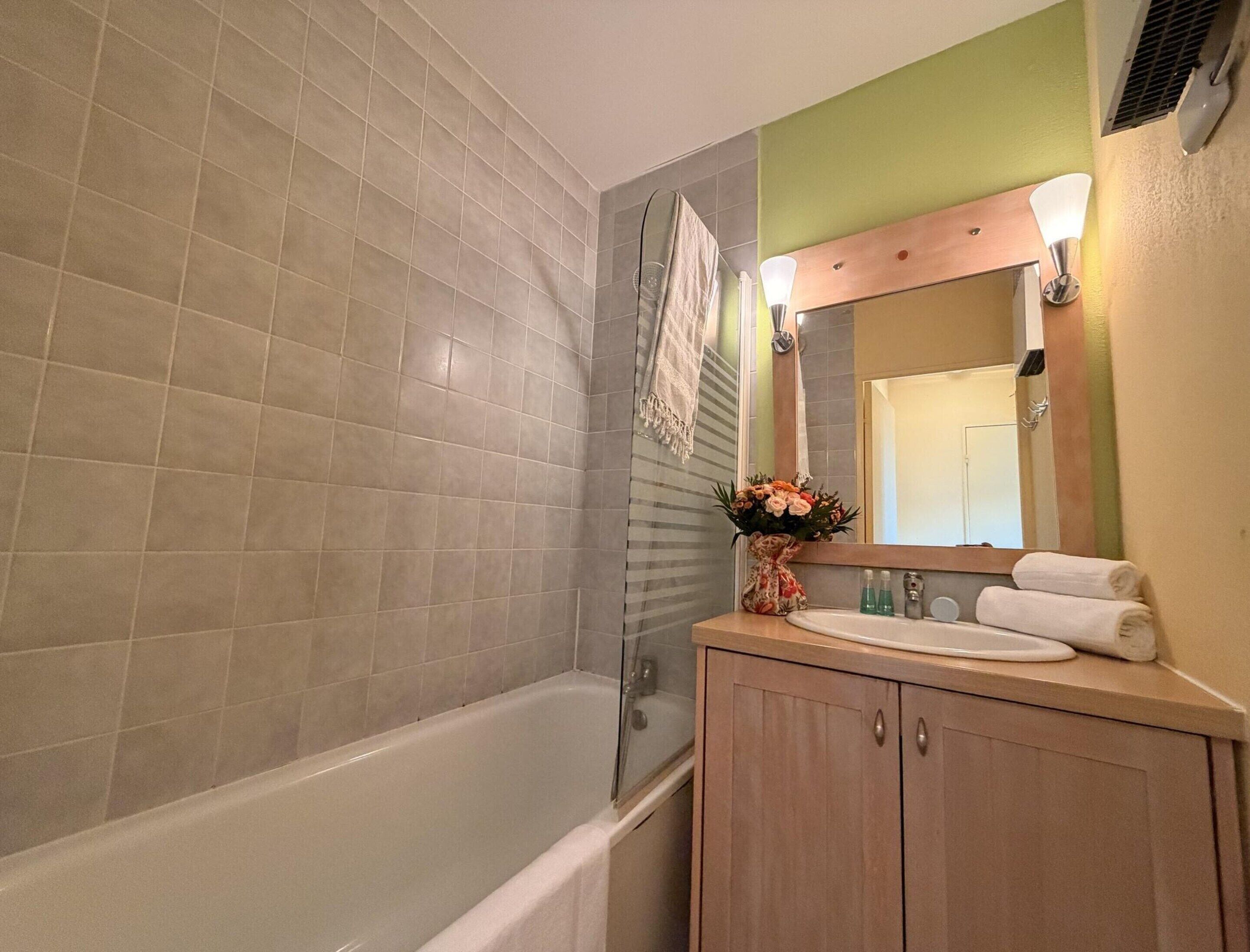 A bathroom with a bathtub, a sink, a mirror, and a towel rack.