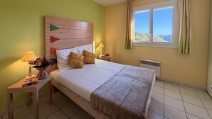 Ein Schlafzimmer mit Bett, Nachttischlampen, einem Fenster mit Vorhängen und Blick ins Freie.