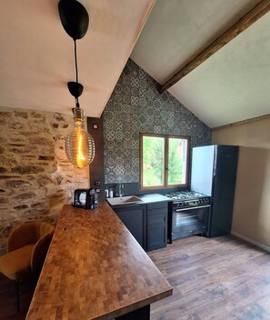 Une cuisine avec un mur en pierre, une table à manger en bois, un luminaire suspendu et une fenêtre offrant une belle vue.