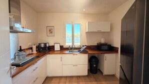 Cocina compacta con encimeras de madera, armarios blancos y un refrigerador de acero inoxidable, además de un ventanal que proporciona luz natural.