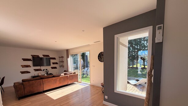 Un salón moderno con suelo de madera, un sofá marrón, un televisor de pantalla plana y un amplio ventanal con vistas al exterior.