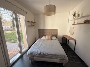 A bedroom with a bed, a bedside table, a hanging light fixture, and a view through the sliding glass door. - House with swimming pool, ideal for vacations & professional stays. (Saint jean d’illac)