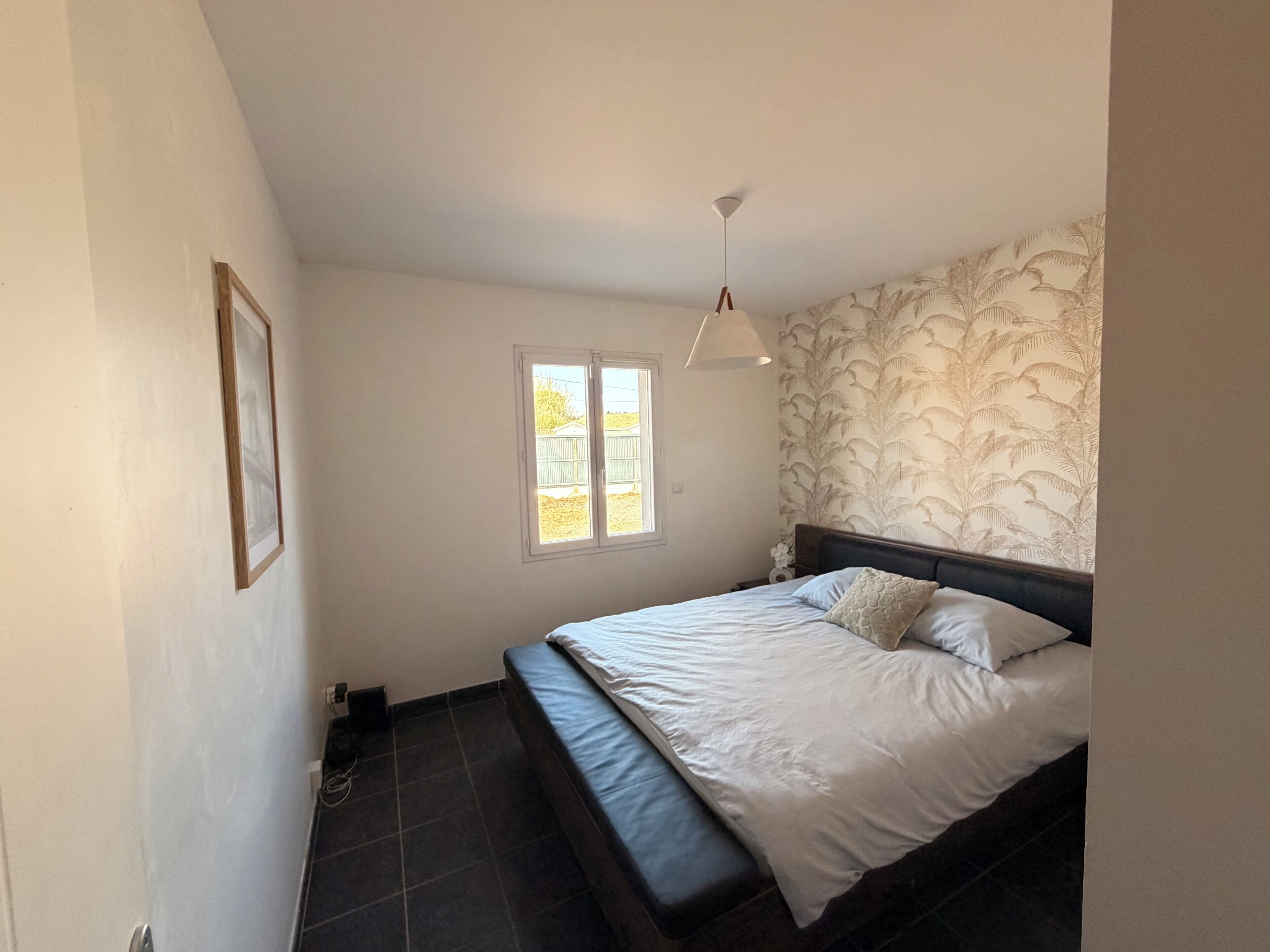 A bedroom with a bed, a window, a ceiling light, and a patterned wall.