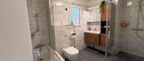 Une salle de bain moderne avec une douche à parois de verre, un lavabo blanc, des toilettes et un mur recouvert de carreaux de marbre.