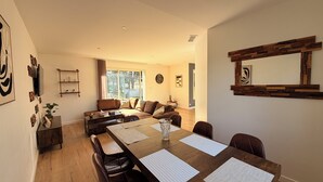 Amplia sala de estar con una gran mesa de comedor de madera, sillas de cuero, un sofá y un televisor.