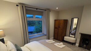 Een slaapkamer met een groot bed, een kledingkast, een spiegel en uitzicht op het omliggende landschap.