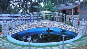 A bridge over a decorative pond with a patterned edge, surrounded by stone walls and greenery. - GGH Maa Samaleshwari Farmhouse (Sambalpur)