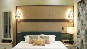 A hotel room with a bed, pillows, a headboard, wall sconces, a nightstand, a lamp, and a curtain. - GGH Maa Samaleshwari Farmhouse (Sambalpur)