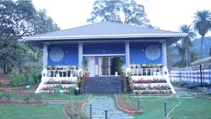 A building with a blue roof and white columns, surrounded by a garden with various plants and flowers. - GGH Maa Samaleshwari Farmhouse (Sambalpur)