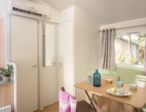 A room with a wooden table, a window with curtains, a potted plant, and a towel hanging on a door. - Adriatic Family Stay by the Sea (Brtonigla)