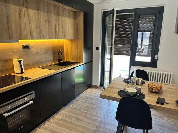 Eine moderne Küche mit Holzarbeitsplatte, schwarzen Schränken, einem eingebauten Backofen und einem Essbereich mit Tisch und Stühlen.