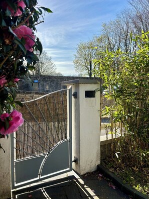 Ein verschlossener Eingang mit einem Metallgitter, einer kleinen Verteilerbox und einer Steinmauer im Hintergrund.