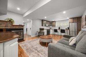 A modern living room with a fireplace, a dining area with bar stools, and a kitchen with stainless steel appliances. - 1 BR Executive Suite | Laundry, Parking & Workspace (Smiths Falls)
