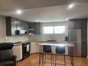 Une cuisine moderne avec des meubles de couleur sombre, un réfrigérateur en acier inoxydable, un four à micro-ondes et un ßlot central en bois avec deux chaises.