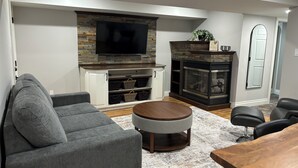 Una sala de estar con televisión de pantalla plana, chimenea, sofás grises y una mesa de centro.
