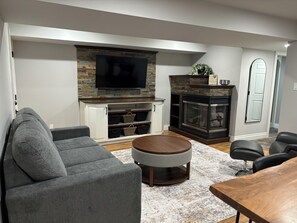 A living room with a flat-screen TV, a fireplace, grey sofas, and a wooden coffee table.