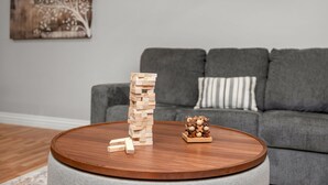 Una sala de estar con un sofá gris, una mesa de centro redonda de madera y una torre de Jenga.