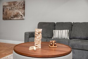 Una sala de estar con un sofá gris, una mesa de centro redonda de madera y una torre de Jenga.