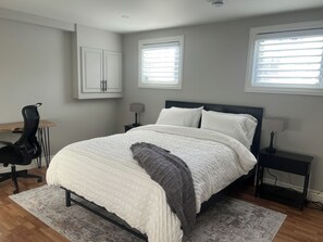 A bedroom with a bed, a desk, a chair, two bedside tables, and a window.