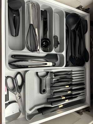 A kitchen drawer with various utensils neatly organized, including whisks, spatulas, and knives.