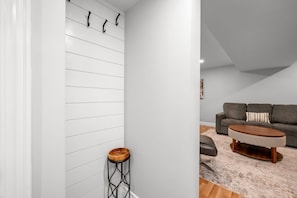 A modern interior with a white wall, a wooden stool, a grey sofa, and a round coffee table. - 1 BR Executive Suite | Laundry, Parking & Workspace (Smiths Falls)