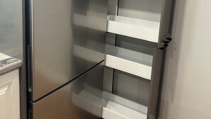 Un refrigerador de acero inoxidable con un estante despensa incorporado, un gabinete blanco arriba y piso de madera.