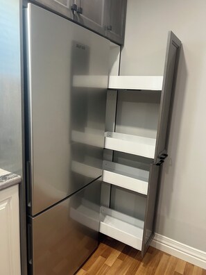 A stainless steel refrigerator with a built-in pantry shelf, a white cabinet above, and a wooden floor.