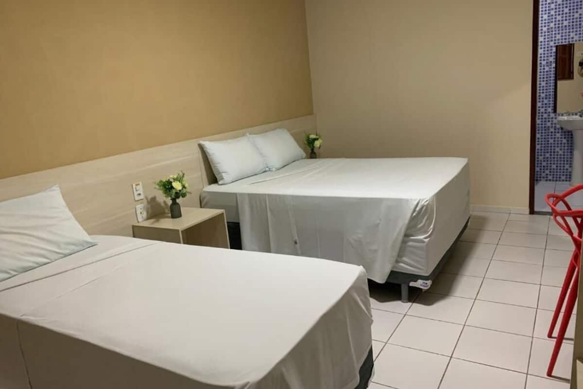 A hotel room with two beds, a small bedside table with a vase, and a red chair.
