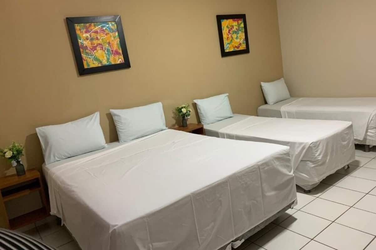 A hotel room with two beds, each with white bedding, a small bedside table with a vase of flowers, and two abstract paintings on the wall.