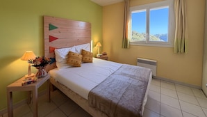Ein Schlafzimmer mit Bett, Nachttischlampen, einem Fenster mit Vorhängen und Blick ins Freie.