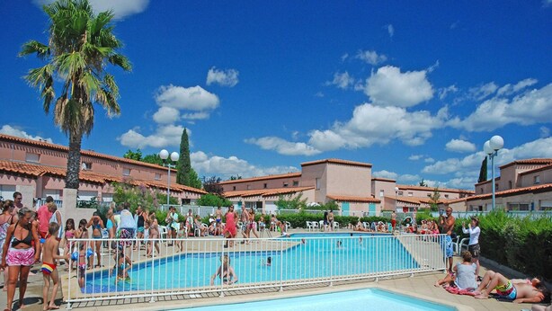 Area piscina con persone, una palma e edifici dai tetti rossi.