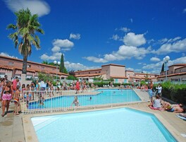 Une piscine entourée de personnes, un palmier et des bâtiments aux toits recouverts de tuiles rouges.