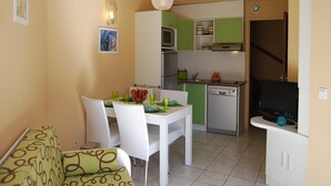 Zona pranzo con tavolo e sedie bianche, cucina con mobili verdi e un televisore su un mobile.