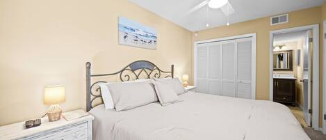 Quarto com cama, mesas de cabeceira, ventoinha no teto, quadro e armário.