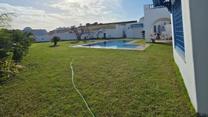 Una piscina, un edificio blanco con detalles azules y un cielo despejado.