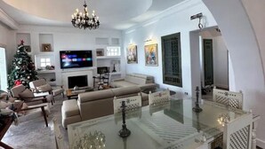 Un espacio habitable amplio con una mesa de comedor de vidrio, una chimenea, un televisor y un árbol de Navidad.