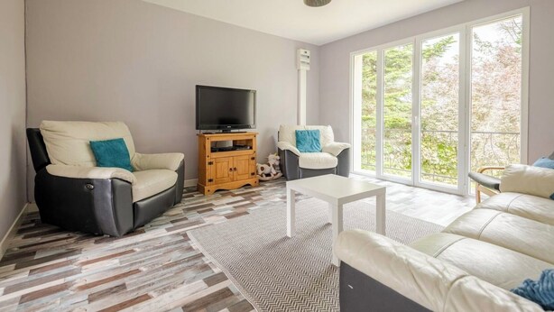 A living room with a sofa, armchair, TV stand, and a view through large windows. - Peace 3 bed gîte (Chevanceaux)
