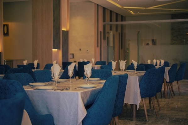 Comedor con mesas dispuestas para el servicio, sillas tapizadas en azul y una paleta de colores neutros.