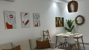 Ein modernes Wohnzimmer mit einer Eckcouch, einem runden Couchtisch, einem Essbereich mit Tisch und Stühlen sowie Wandbildern.