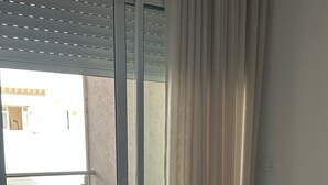 Ein Zimmer mit einer Schiebeglastür, die auf einen Balkon führt, einem runden Tisch mit Kerze und einer Couch mit gemusterten Kissen.