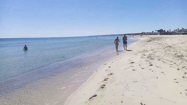 Ein Strand mit blauem Himmel, ruhigem Wasser und Fußabdrücken im Sand.