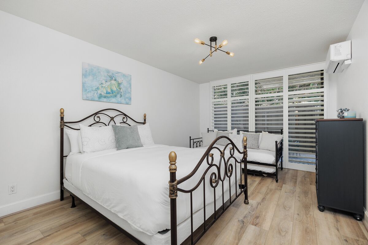 A bedroom with a bed, a desk, a chair, a wardrobe, and a window with blinds.