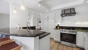 Een moderne keuken met een centraal eiland, roestvrijstalen apparatuur en hanglampen.