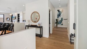 Un intérieur moderne comprenant un coin repas, une console avec un miroir, un escalier et un grand tableau abstrait.