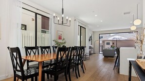 Un coin repas avec une table en bois et des chaises noires, un lustre et une vue sur un balcon doté d’une balustrade.