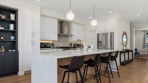 Une cuisine moderne avec des meubles blancs, un îlot central doté de tabourets et des luminaires suspendus.