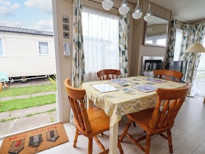 Uma sala de jantar com uma mesa posta para quatro pessoas, cadeiras de madeira, toalha de mesa estampada e vista para uma casa lá fora.